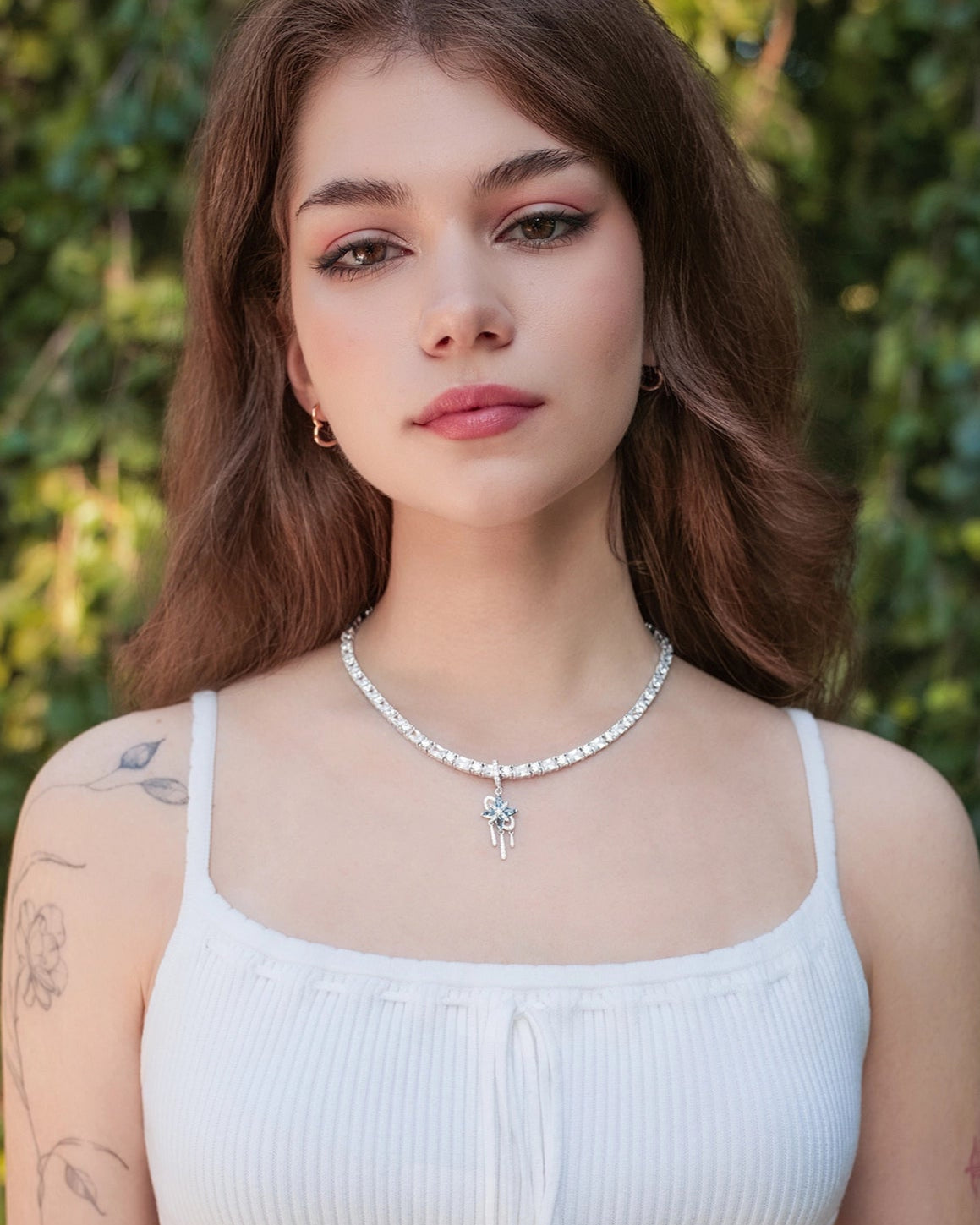 Woman wearing a white sleeveless top with a green leafy background