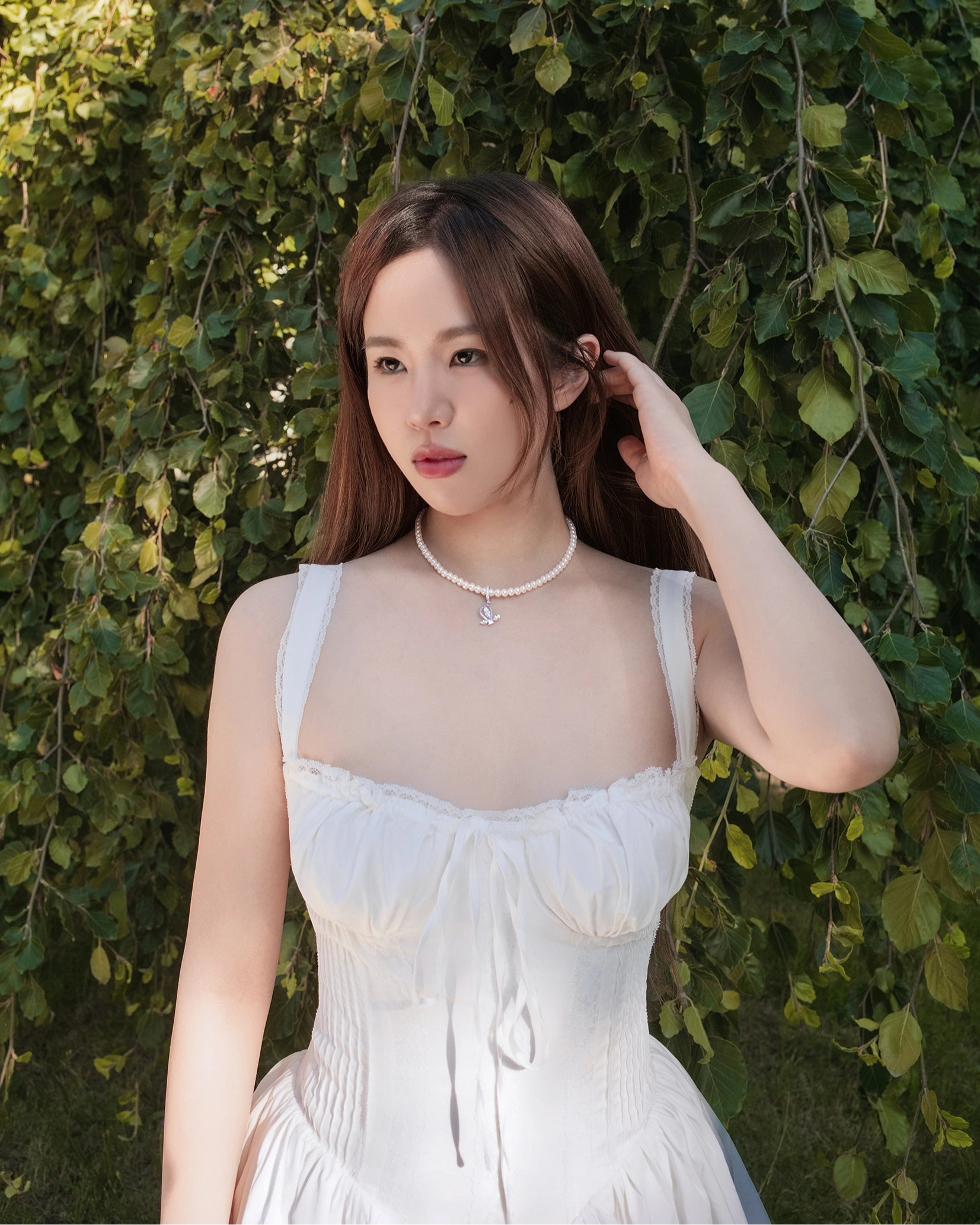 Woman in a white dress standing against a green leafy background
