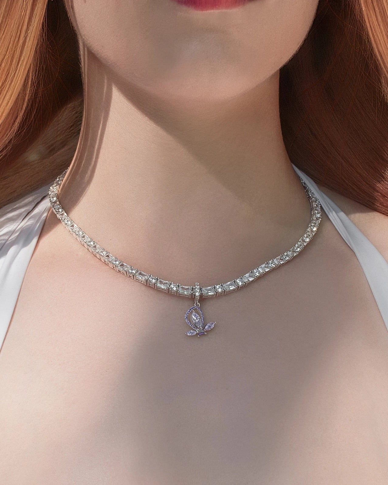 Close-up of a necklace with a pendant on a person wearing a white top outdoors.