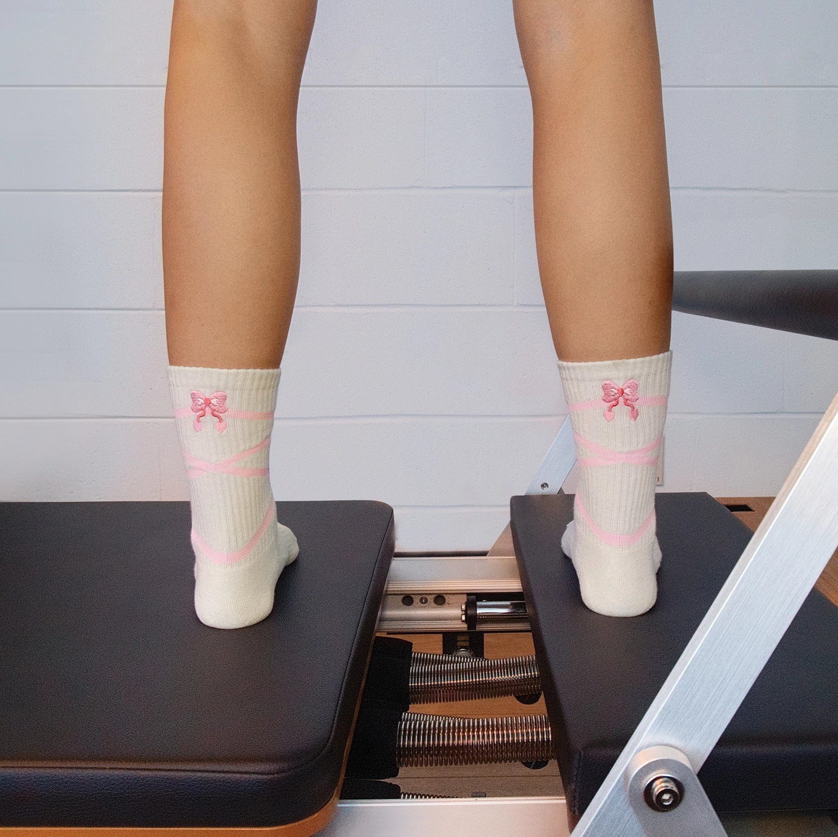 Person wearing white socks with pink designs on a Pilates reformer machine.