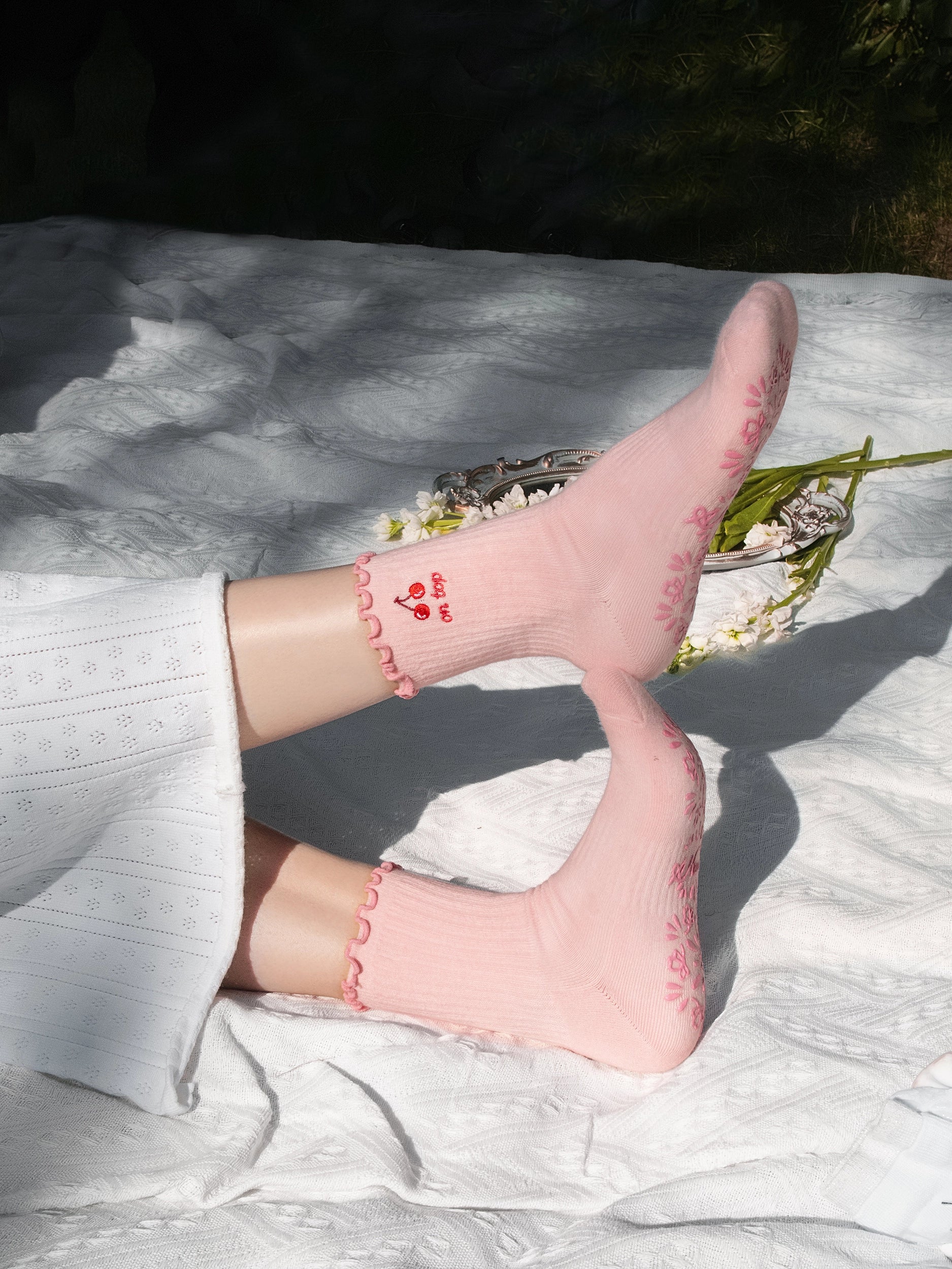 Pink socks with heart design on a white surface with greenery