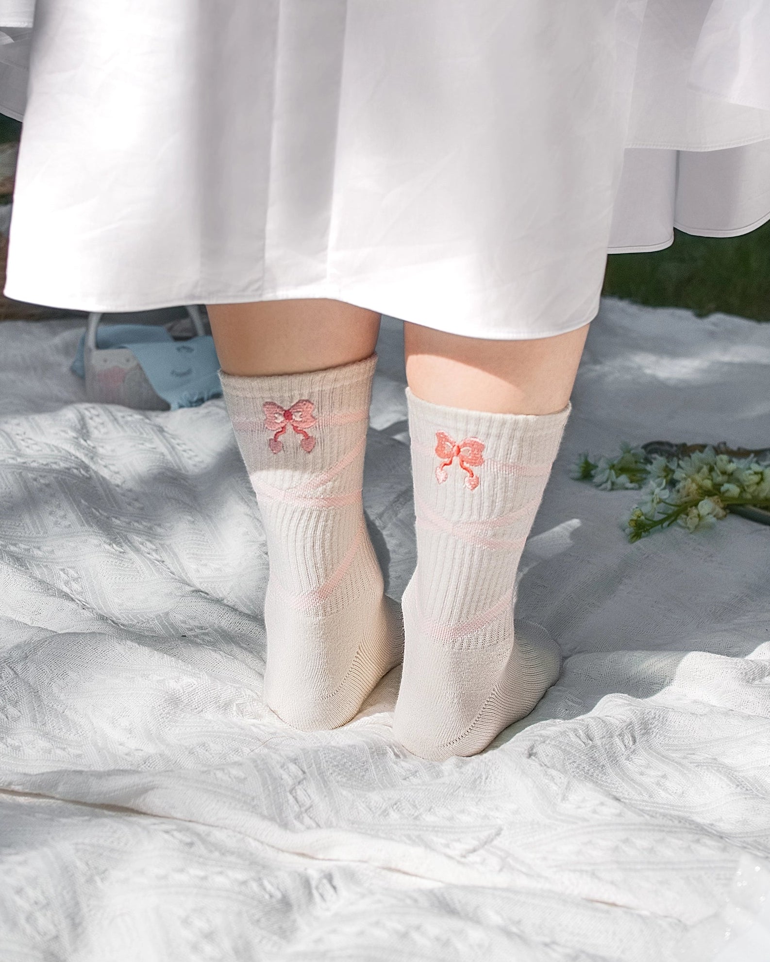 White socks with pink butterfly designs worn by a person in a white dress on a white surface.